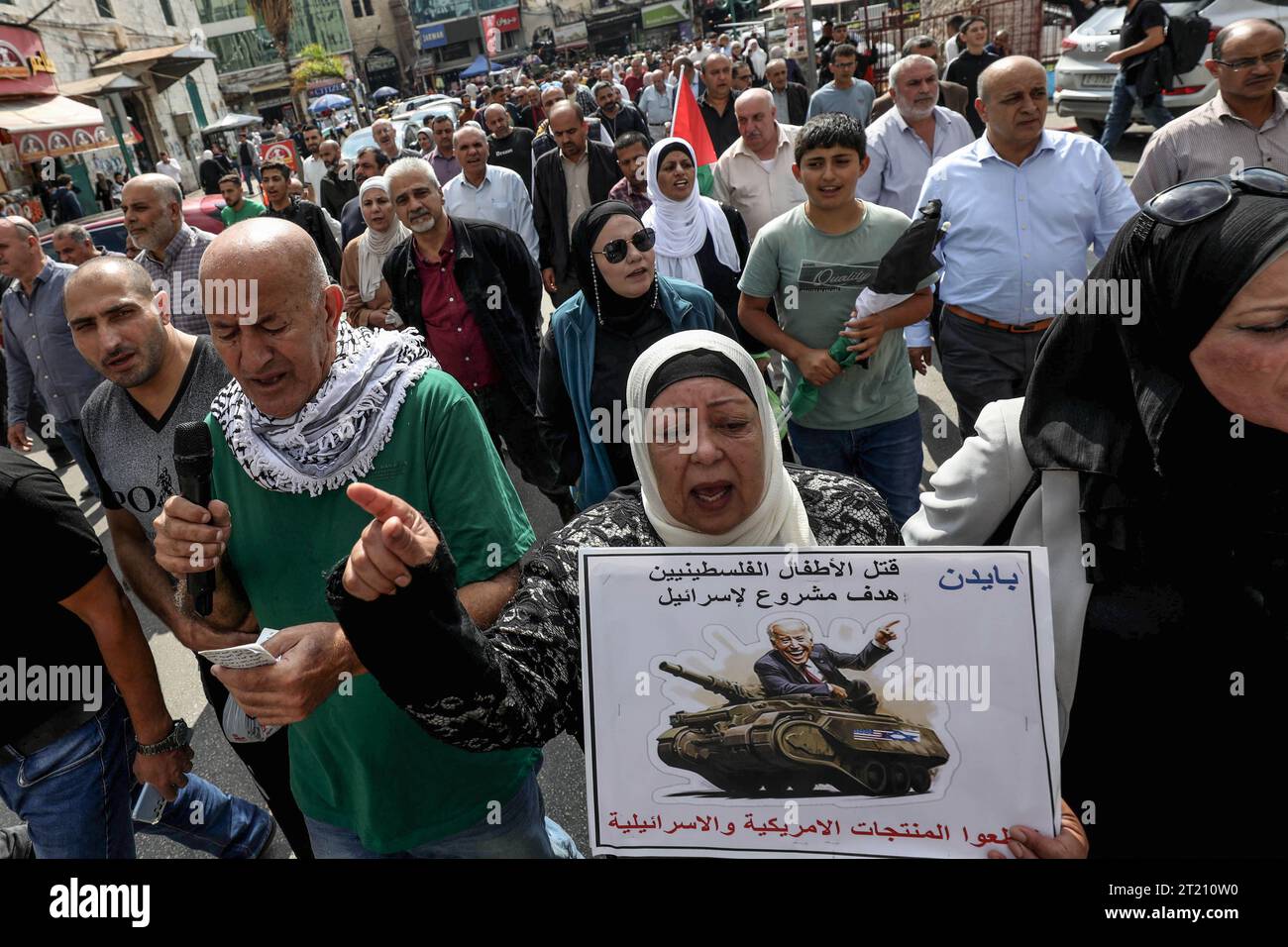 Nablus, territori palestinesi. 16 ottobre 2023. Un manifestante palestinese tiene in mano un cartello raffigurante il presidente degli Stati Uniti Joe Biden che cavalca su un carro armato militare con un testo arabo che recita: "Uccidere bambini palestinesi è un obiettivo legittimo per Israele” e "boicottare i prodotti statunitensi e israeliani”, durante una manifestazione contro Israele e gli Stati Uniti nella città di Nablus in Cisgiordania. Credito: Ayman Nobani/dpa/Alamy Live News Foto Stock