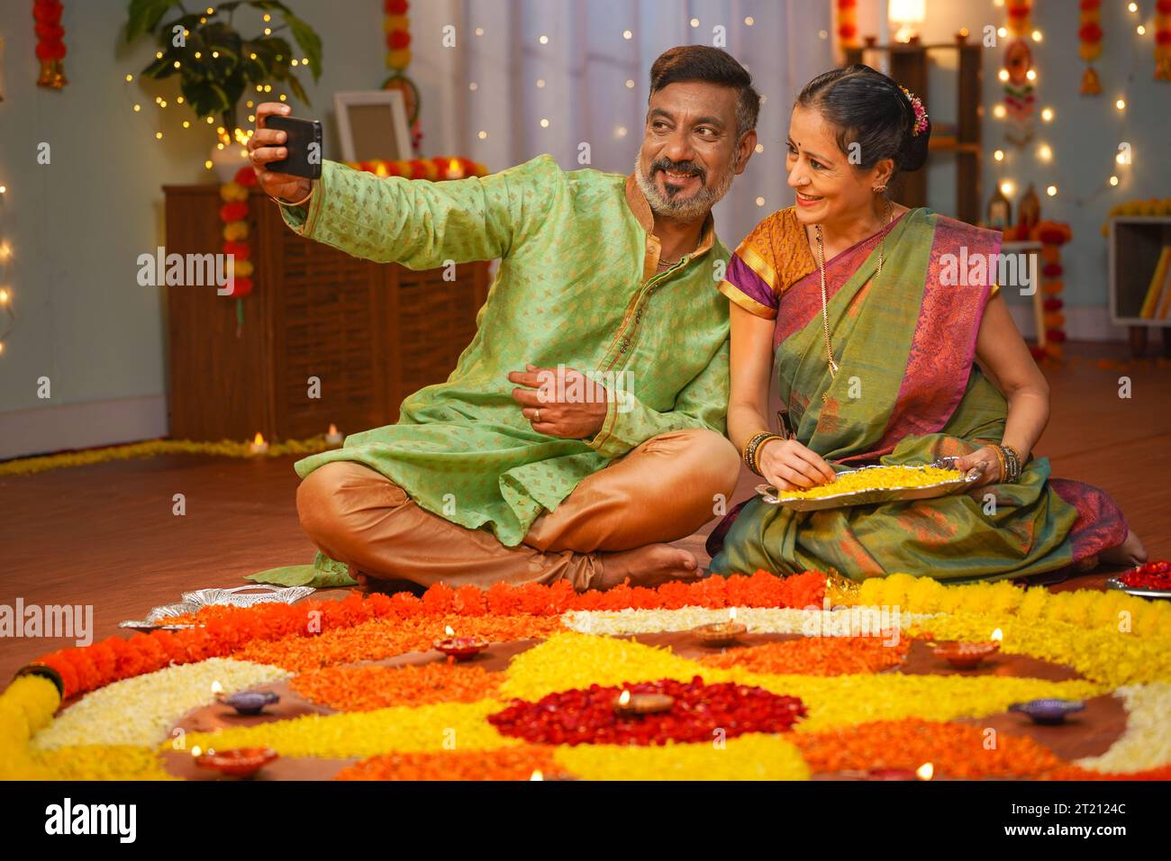 coppia anziana che si prende selfie durante la preparazione festiva di diwali a casa di fronte ai rangoli di fiori - concetto di condivisione sui social media, famiglia Foto Stock