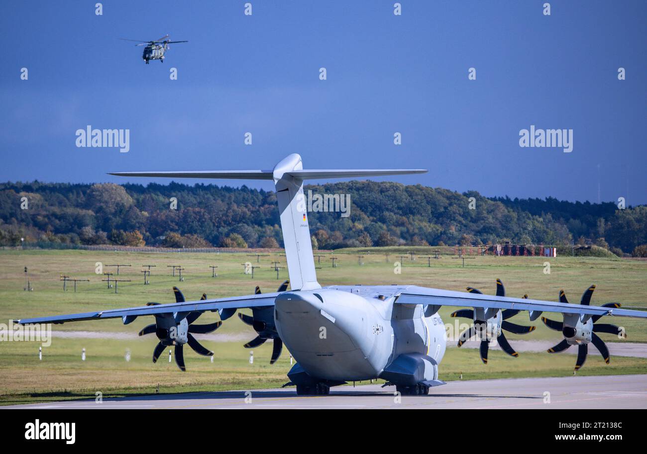 Laage, Germania. 16 ottobre 2023. Un elicottero militare NH-90 vola sopra l'aeroporto del Tactical Air Wing 73 'Steinhoff' sul cui piazzale un aereo da trasporto Airbus A400M è parcheggiato durante l'esercitazione 'Baltic Hunter 2023'. Un totale di 50 aerei saranno in azione nelle prossime due settimane. Secondo la Bundeswehr, i complessi scenari di esercitazione includono attacco aereo, difesa aerea, trasporto aereo tattico e rifornimento aereo. Credito: Jens Büttner/dpa/Alamy Live News Foto Stock