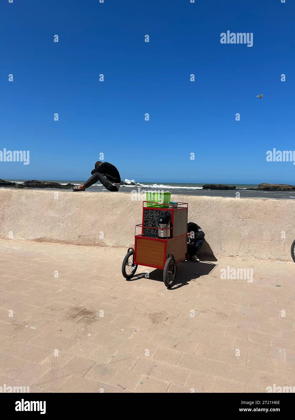 Una ciclista è tranquilla in bicicletta lungo una spiaggia sabbiosa passando davanti a un chiosco di distributori automatici sulla spiaggia Foto Stock