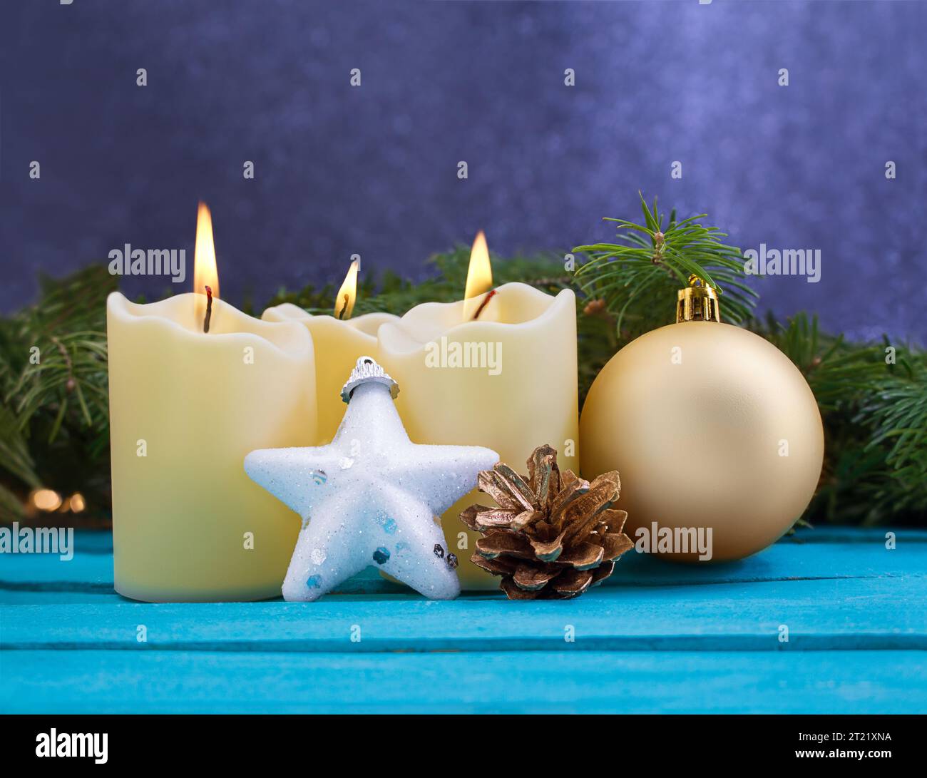 Candele di Natale con fuoco, stella bianca scintillante, cono di pino dorato e palla su sfondo di legno blu. Dietro ci sono rami di abete rosso. Anno nuovo. Co Foto Stock