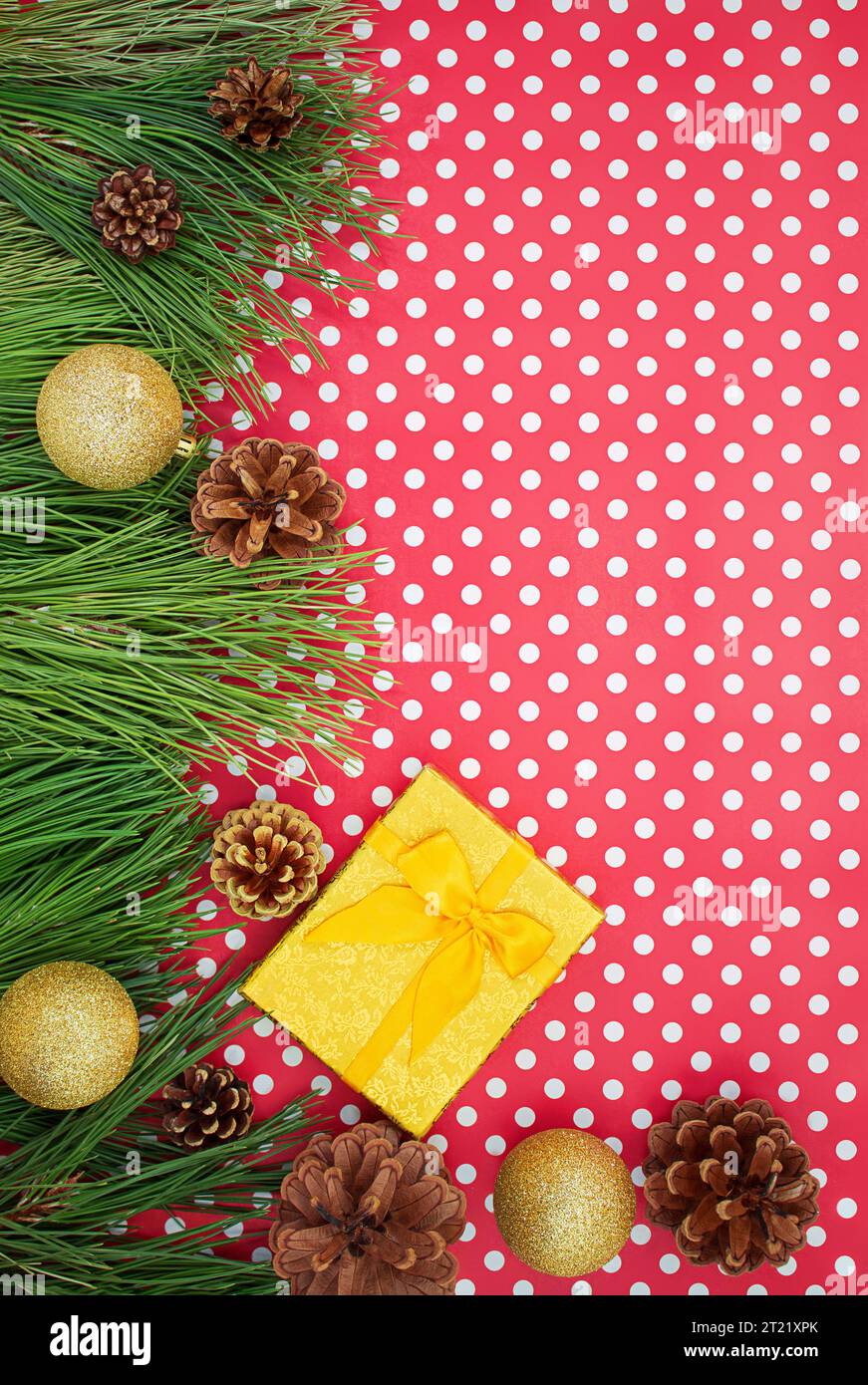 Confezione regalo giallo dorato con fiocco, rami di abete con coni di pino e palline lucide su sfondo bianco rosso con pois. Natale, Capodanno, compleanno. C Foto Stock