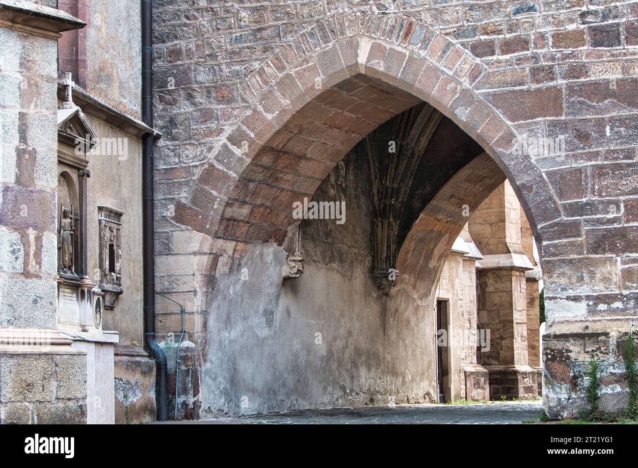 Un'entrata ad arco fatta di vecchia costruzione in mattoni, con due finestre su entrambi i lati e vigne verdi di edera che crescono sulla porta Foto Stock