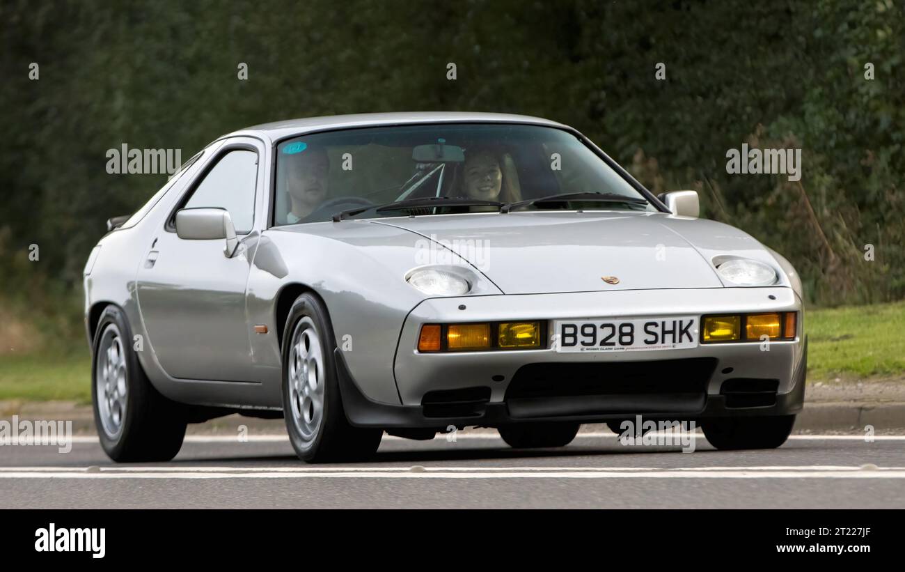 Bicester, Oxon., UK - 8 ottobre 2023: 1984 auto d'epoca Porsche 928 S argento che guida su una strada di campagna inglese. Foto Stock