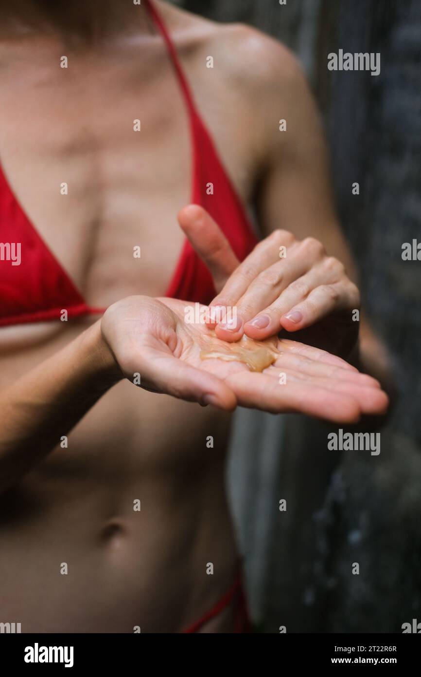 Foto verticale di una donna sotto la doccia che strizza il gel doccia fuori da un vaso e che le prende le mani. Schiuma da gel doccia e sapone nel palmo della donna Foto Stock