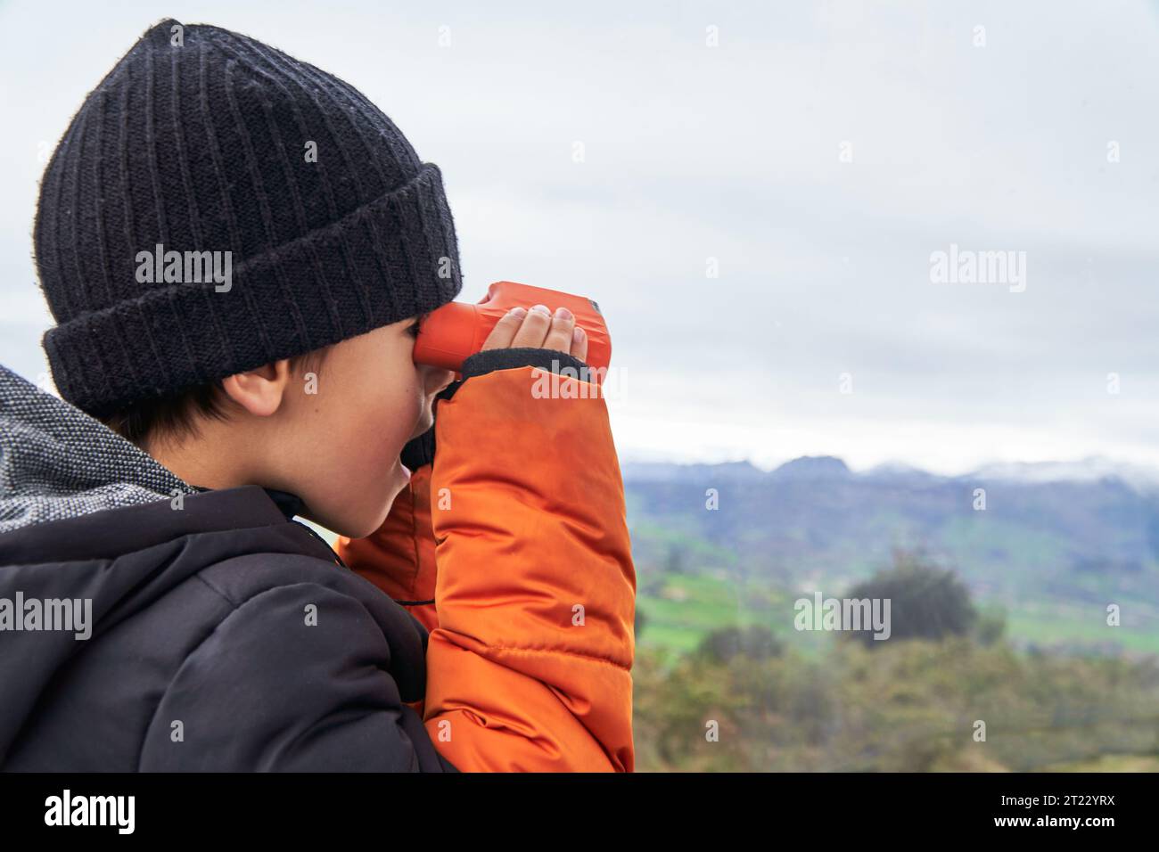 Un bambino sorpreso che guardava con un binocolo durante le vacanze invernali Foto Stock