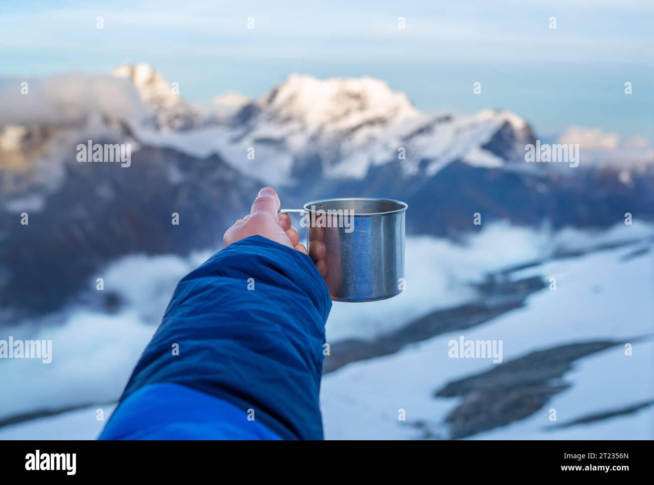 Giovane donna che tiene in mano una tazza di tè caldo in metallo al tramonto dall'accampamento alto di Mera Peak con montagne innevate di sette millesimi. Spedizione di arrampicata conf Foto Stock