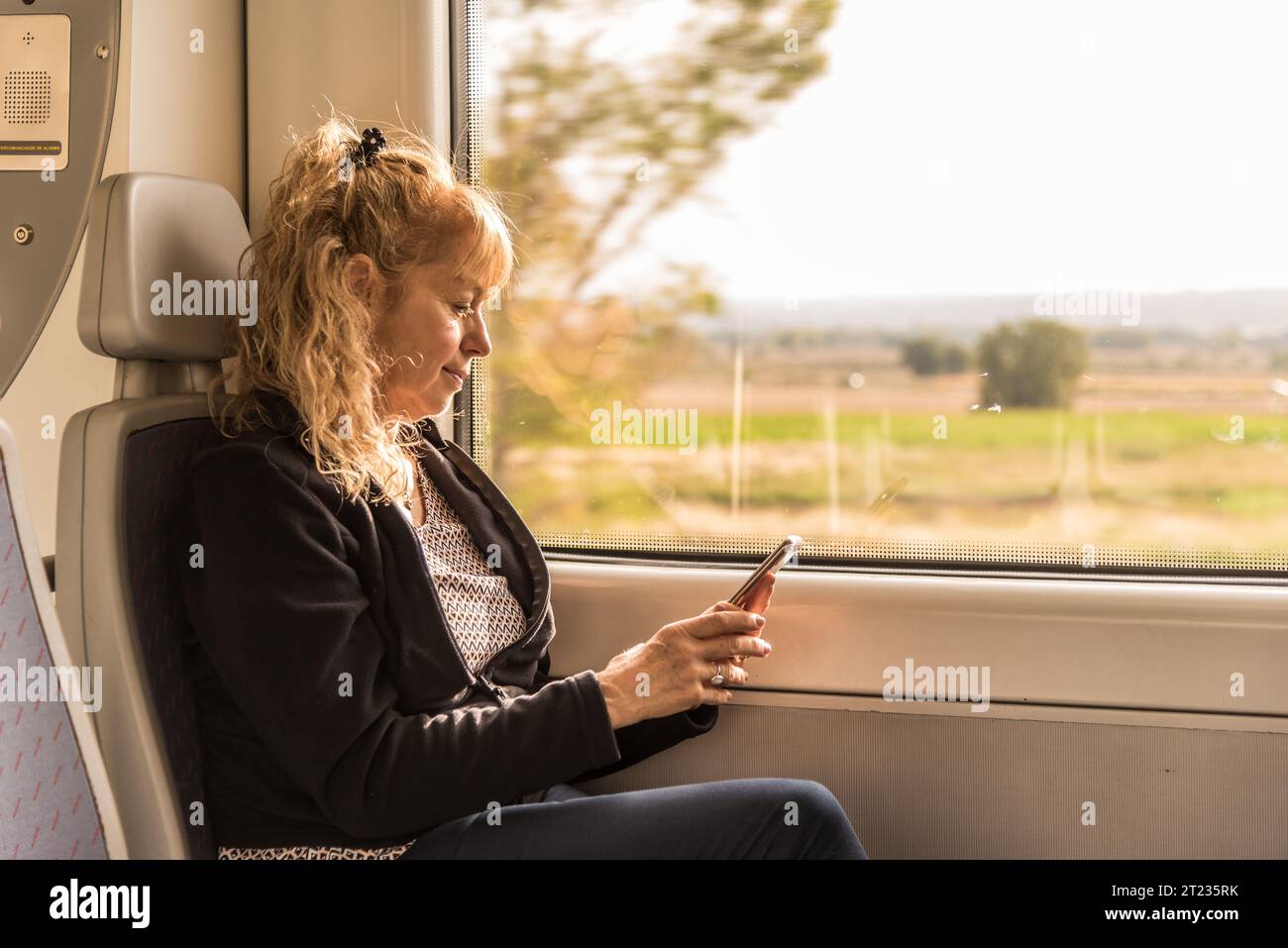 Donna matura che viaggia da sola sul treno e guarda un cellulare. Concetto di viaggio Foto Stock