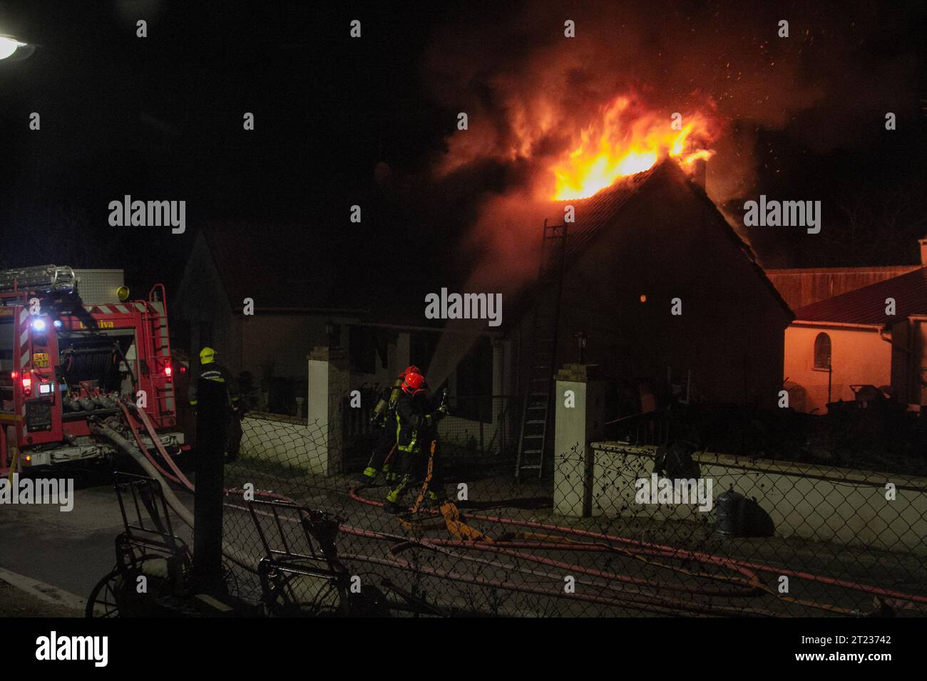 I pompieri a piedi usano un tubo dell'acqua per affrontare le fiamme che consumano il tetto di una casa di un villaggio in Francia. Foto Stock