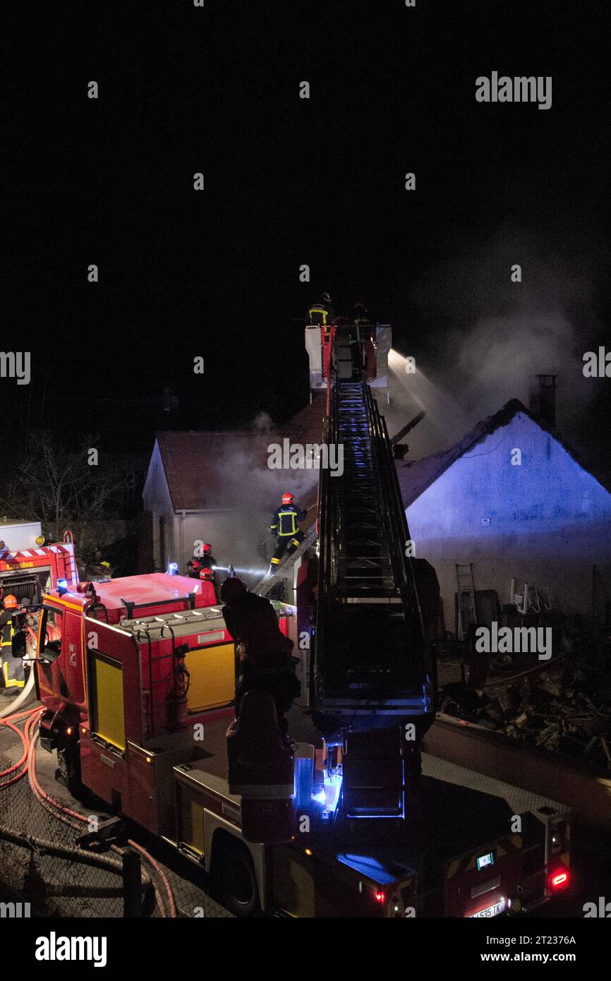 Il pompiere assiste a un incendio di notte in un villaggio in Francia con le macchine antincendio e una scala aerea. Foto Stock