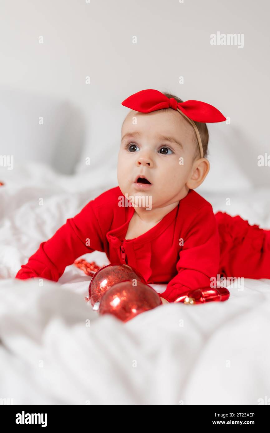 Carino e felice bambino con una tuta rossa è sdraiato sullo stomaco a letto Foto Stock