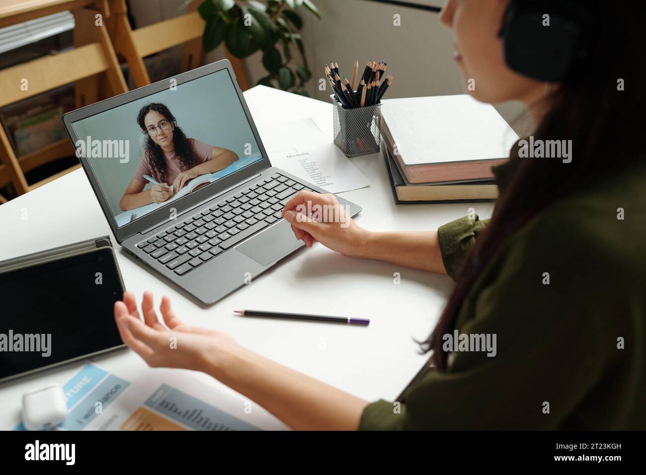 Concentrati sullo schermo del notebook con una studentessa intelligente che prende appunti nel copybook e ascolta la spiegazione dell'argomento da parte dell'insegnante durante la lezione online Foto Stock