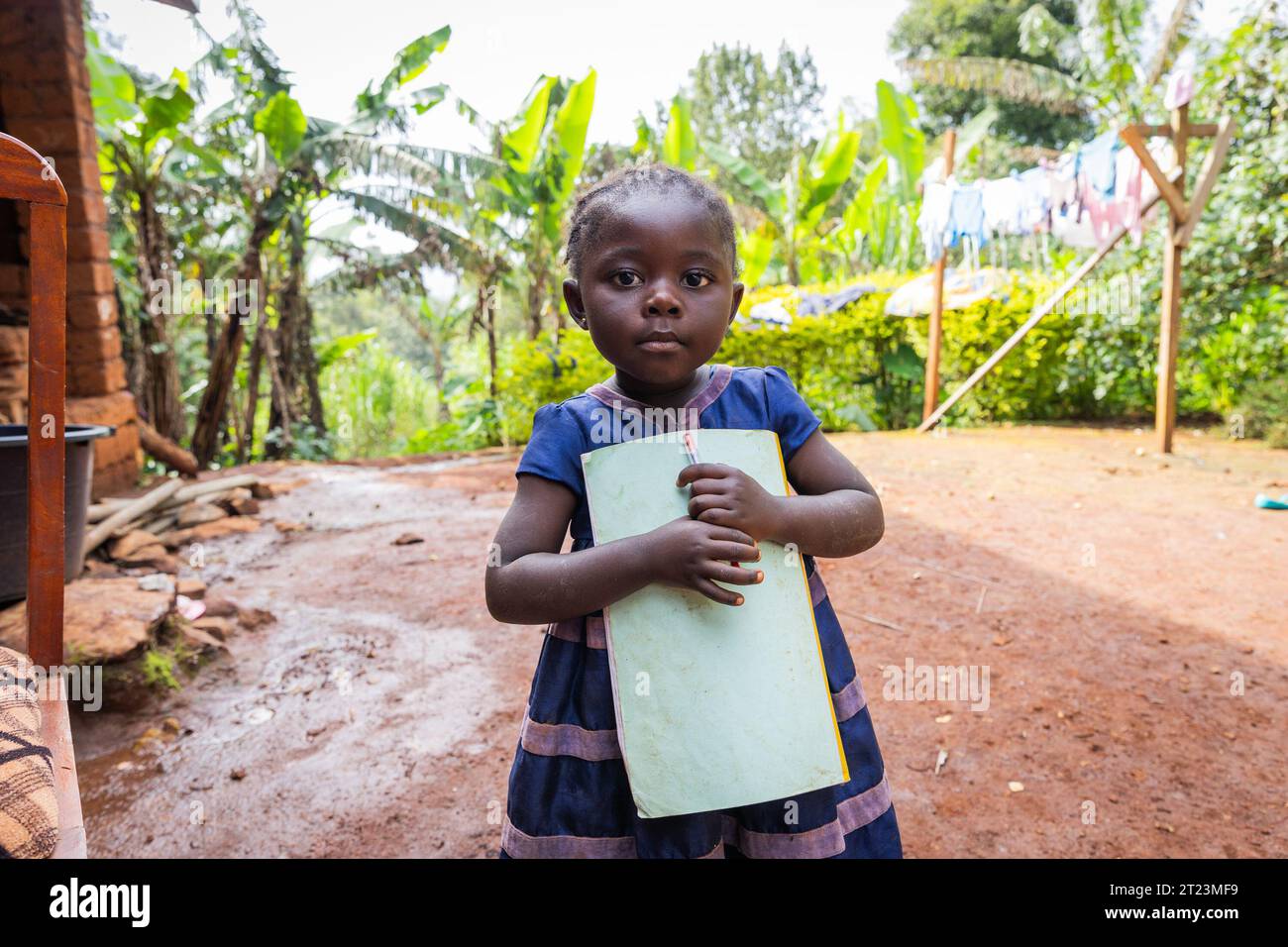Piccola timida bambina che tiene un notebook e una penna tra le braccia all'aperto nel villaggio. Foto Stock