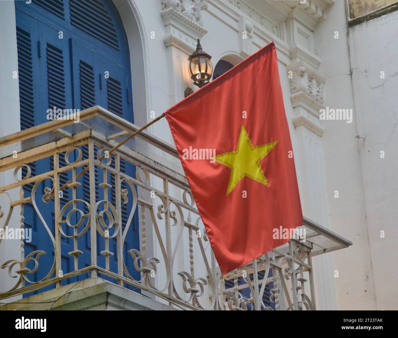Bandiera nazionale rossa d'oro del Vietnam che sventola con orgoglio dal balcone di una casa nello stile coloniale francese del quartiere vecchio di Hanoi Foto Stock