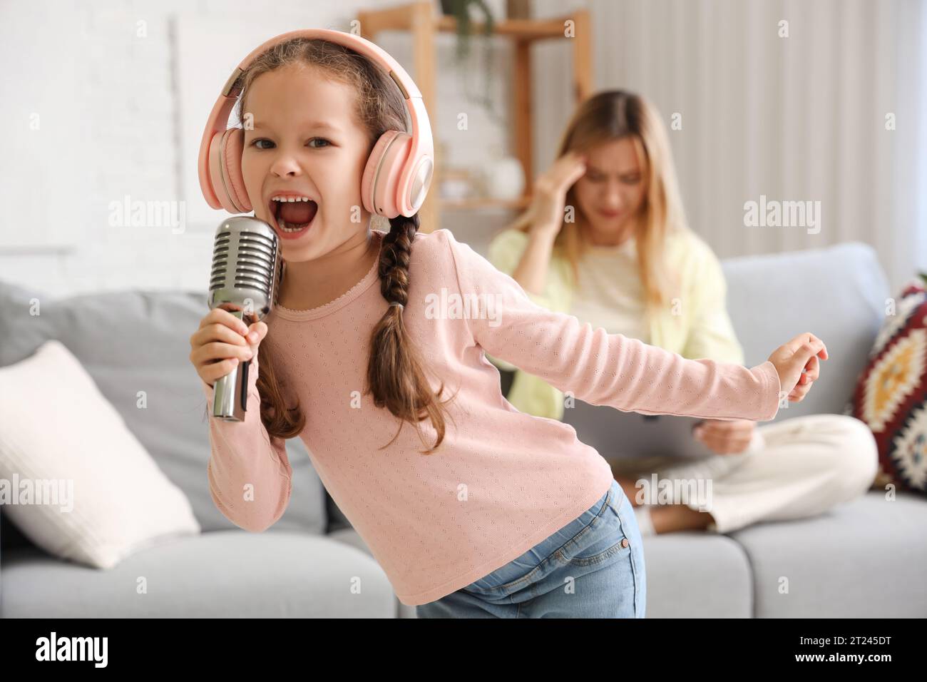 Bambina rumorosa in cuffie con microfono che canta a casa Foto Stock