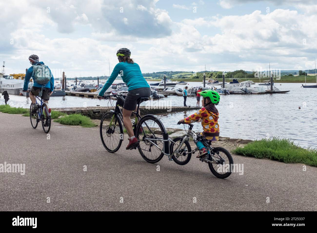 Mamma in bicicletta con la bicicletta per bambini attaccata dietro, Topsham, Devon, Regno Unito Foto Stock