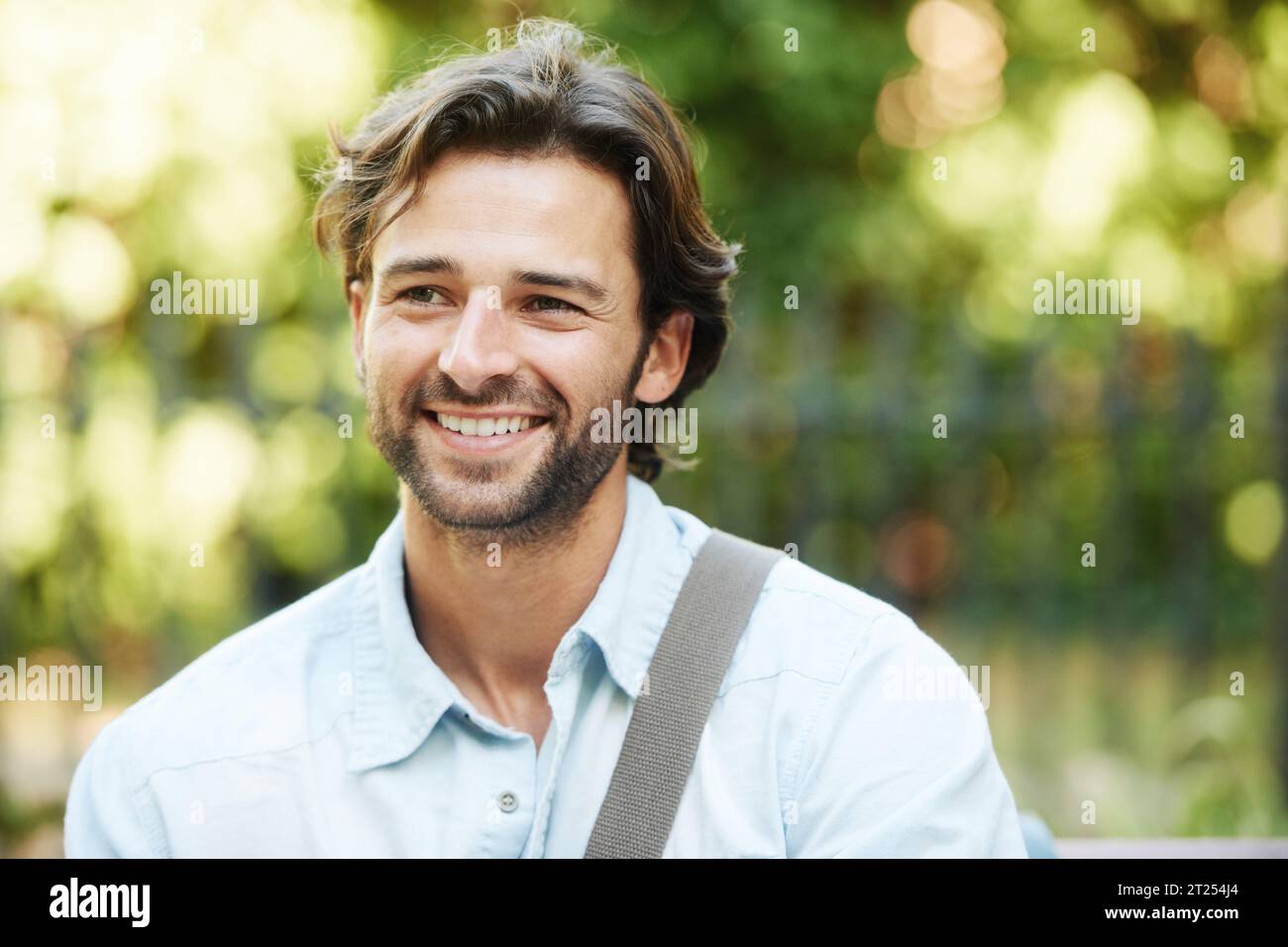 Rilassati, sorridi o un uomo felice in un parco in panchina in estate per una vacanza o una pausa in giardino. Salute mentale, pensiero o volto della persona in natura Foto Stock