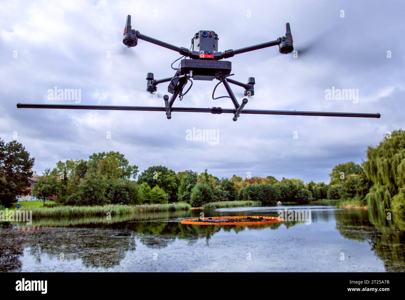 17 ottobre 2023, Meclemburgo-Pomerania occidentale, Rostock: Un drone con sonde per rilevare campi magnetici o anomalie sul fondo del lago vola sopra lo stagno dei cigni durante i voli di misurazione. Le immagini possono essere utilizzate per identificare e individuare eventuali ordigni nel fango. Dal momento che lo stagno è stato creato nel 1938 prima della seconda guerra mondiale, vi è il sospetto di contaminazione da ordigni esplosivi. Foto: Jens Büttner/dpa Foto Stock