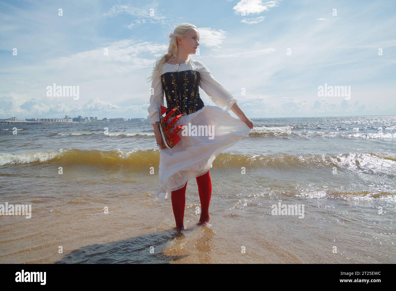 Giovane donna elegante con abito in stile retrò in posa sulla spiaggia di mare contro il cielo Foto Stock