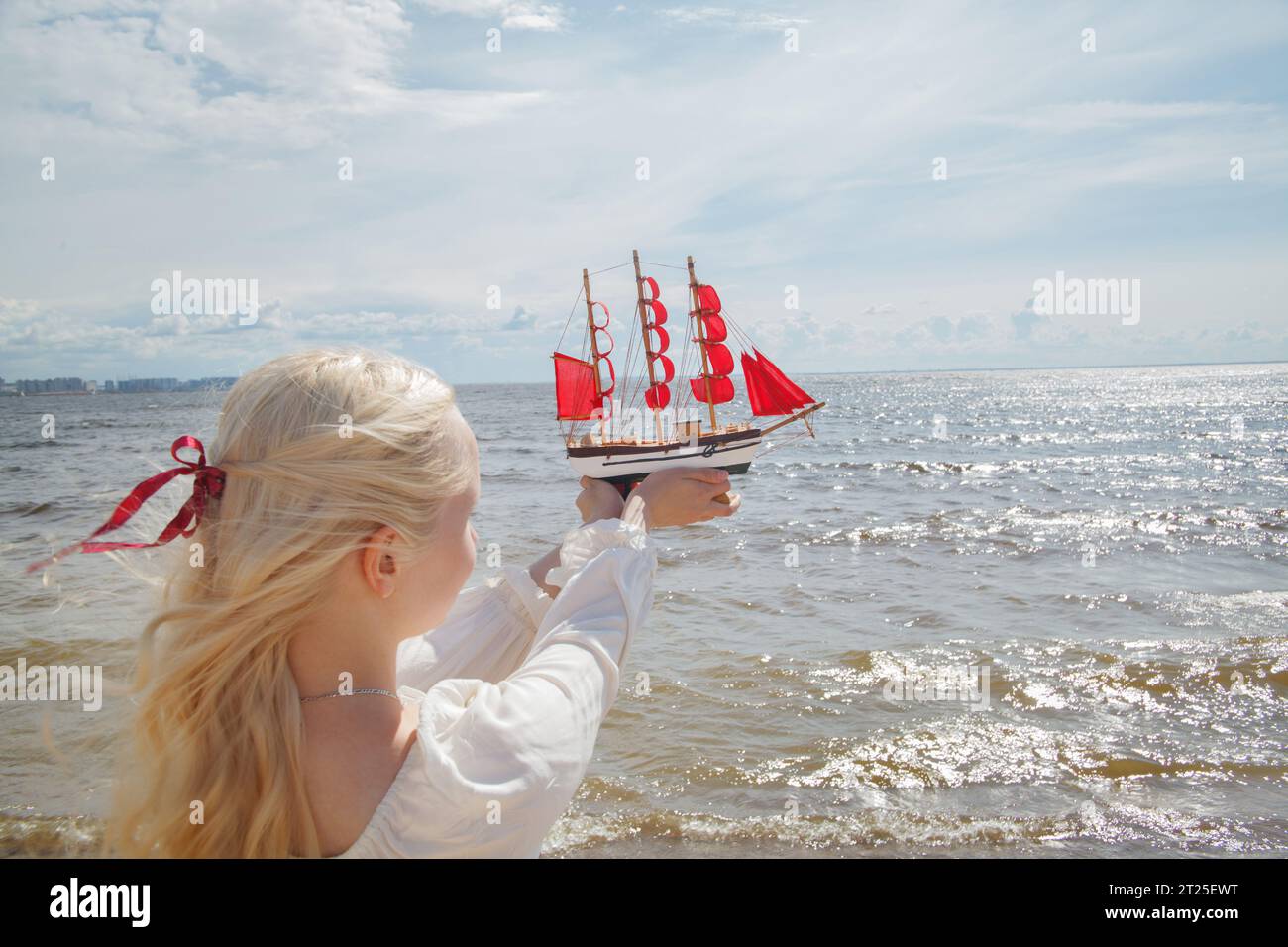 Giovane donna di bellezza che regge una barca a vela rossa contro il mare e il cielo. Concetto di vacanza romantica Foto Stock