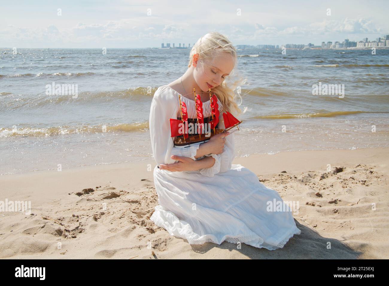 Attraente giovane donna con capelli biondi in abito bianco che sogna sulla spiaggia di mare, ritratto all'aperto Foto Stock