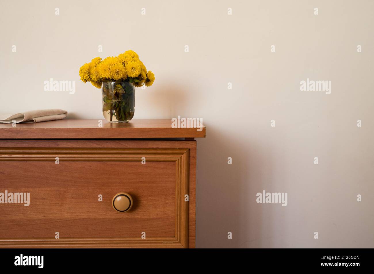 Armadio in legno con vaso di fiori gialli e pezzo di materiale bianco. Arredamento, interni, stile, natura morta Foto Stock