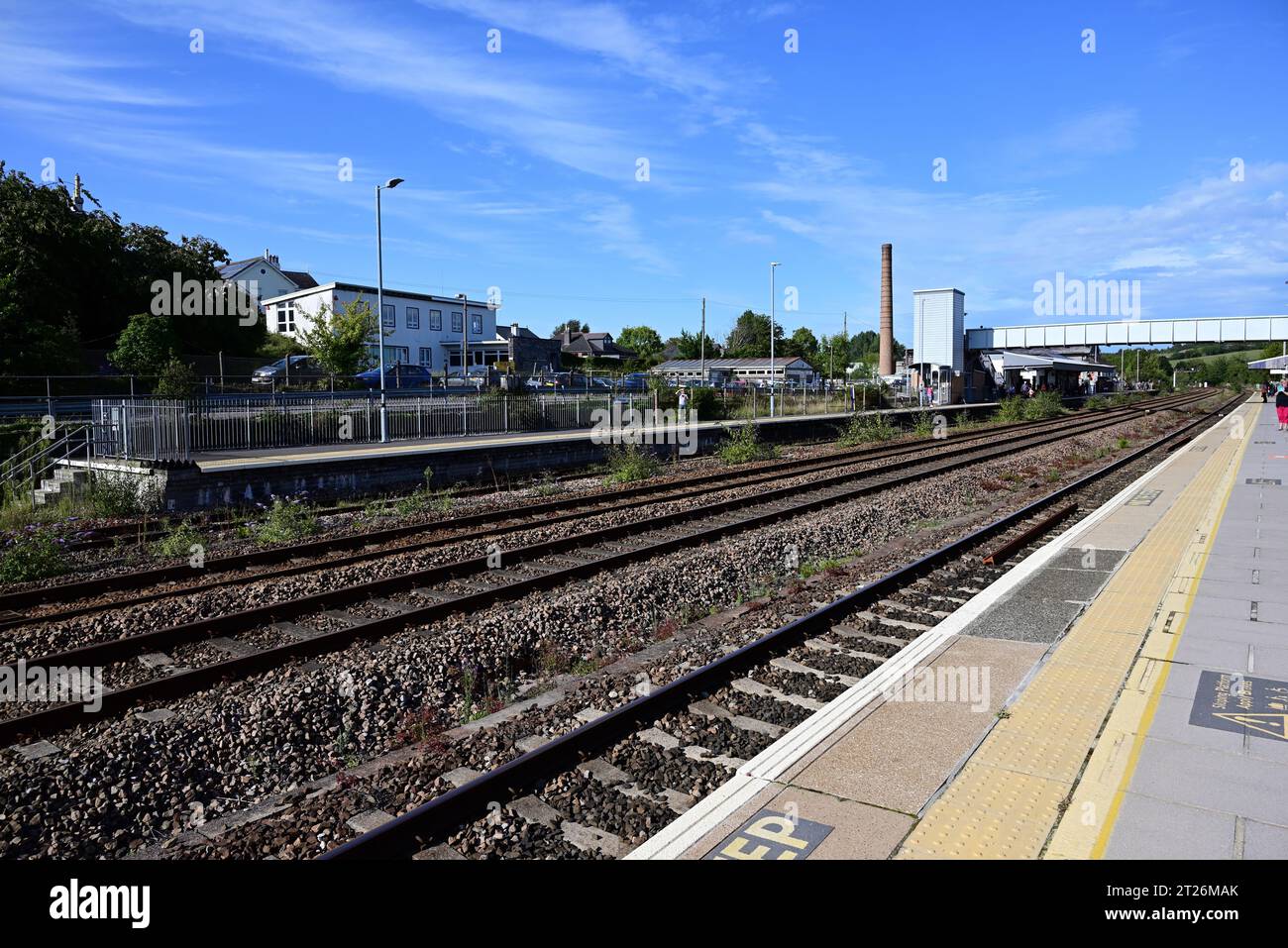 Totnes Station, South Devon, guardando a est verso la passerella pedonale e il camino in disuso dell'ex stabilimento di Dairy Crest. Foto Stock
