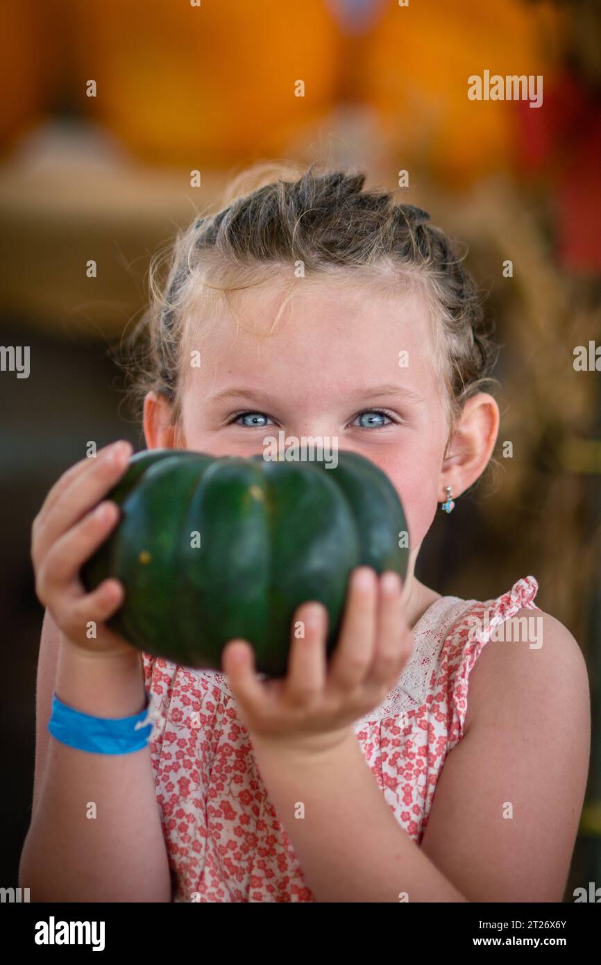 Ritratto ravvicinato di una bambina che tiene in mano una zucca verde in un'area di zucca nella fattoria Deluca, San Pedro, CA Foto Stock