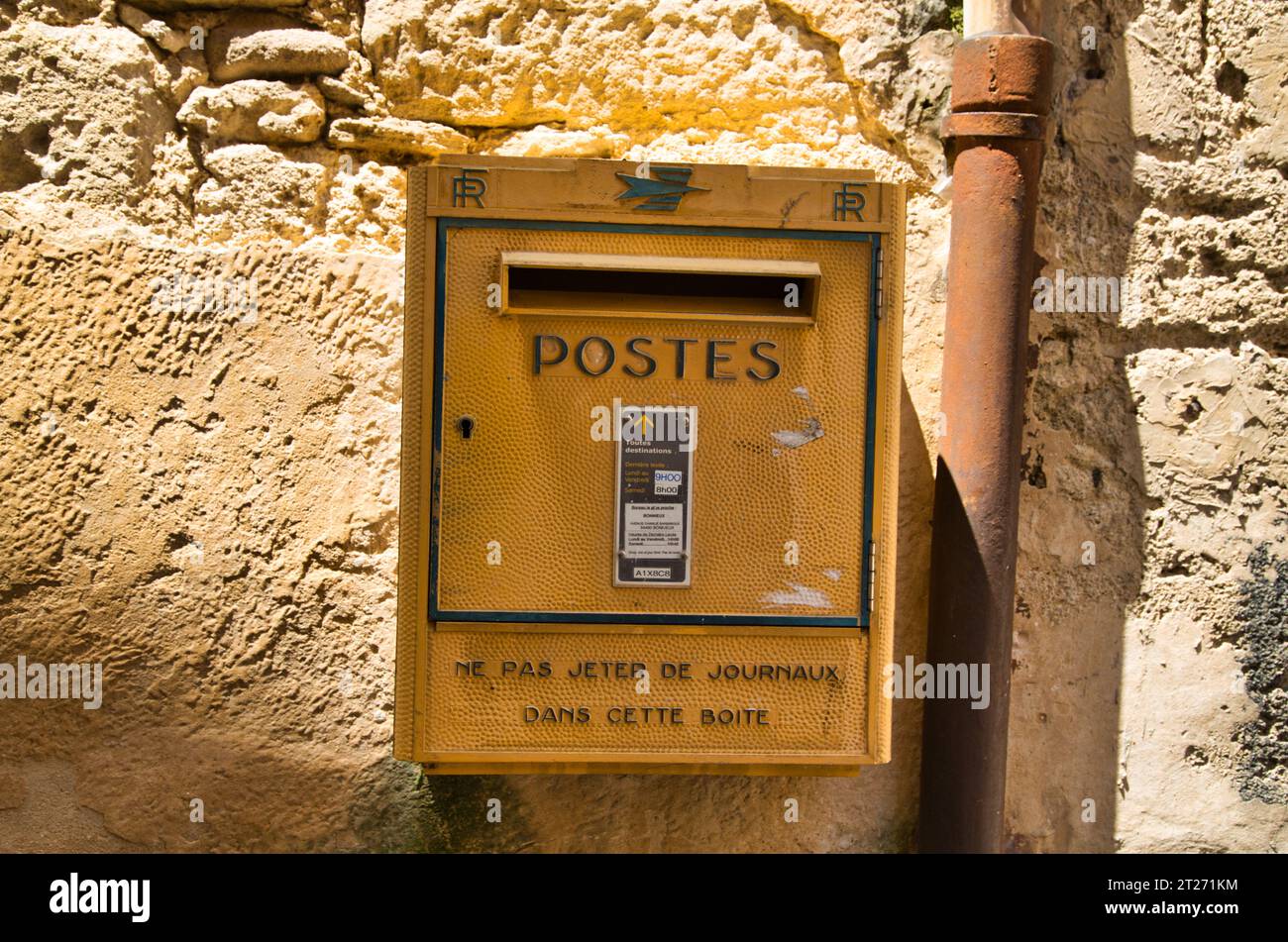 Una cassetta postale gialla d'epoca contro un muro di pietra testurizzata in Provenza, Francia. Foto Stock