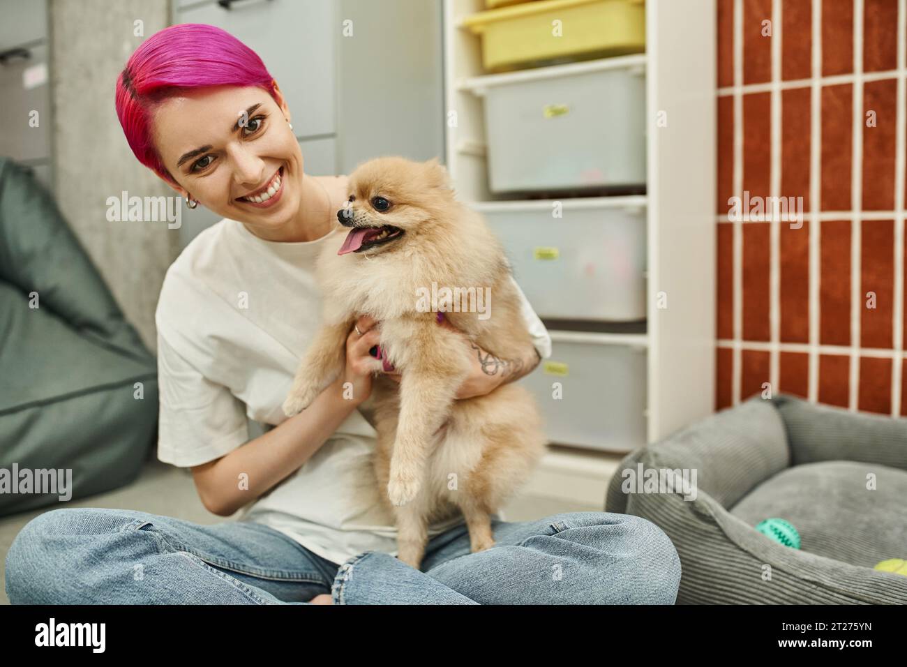 la dog sitter allegra ed elegante abbraccia il pomeranian spitz mentre guardi la macchina fotografica in un hotel per animali domestici Foto Stock