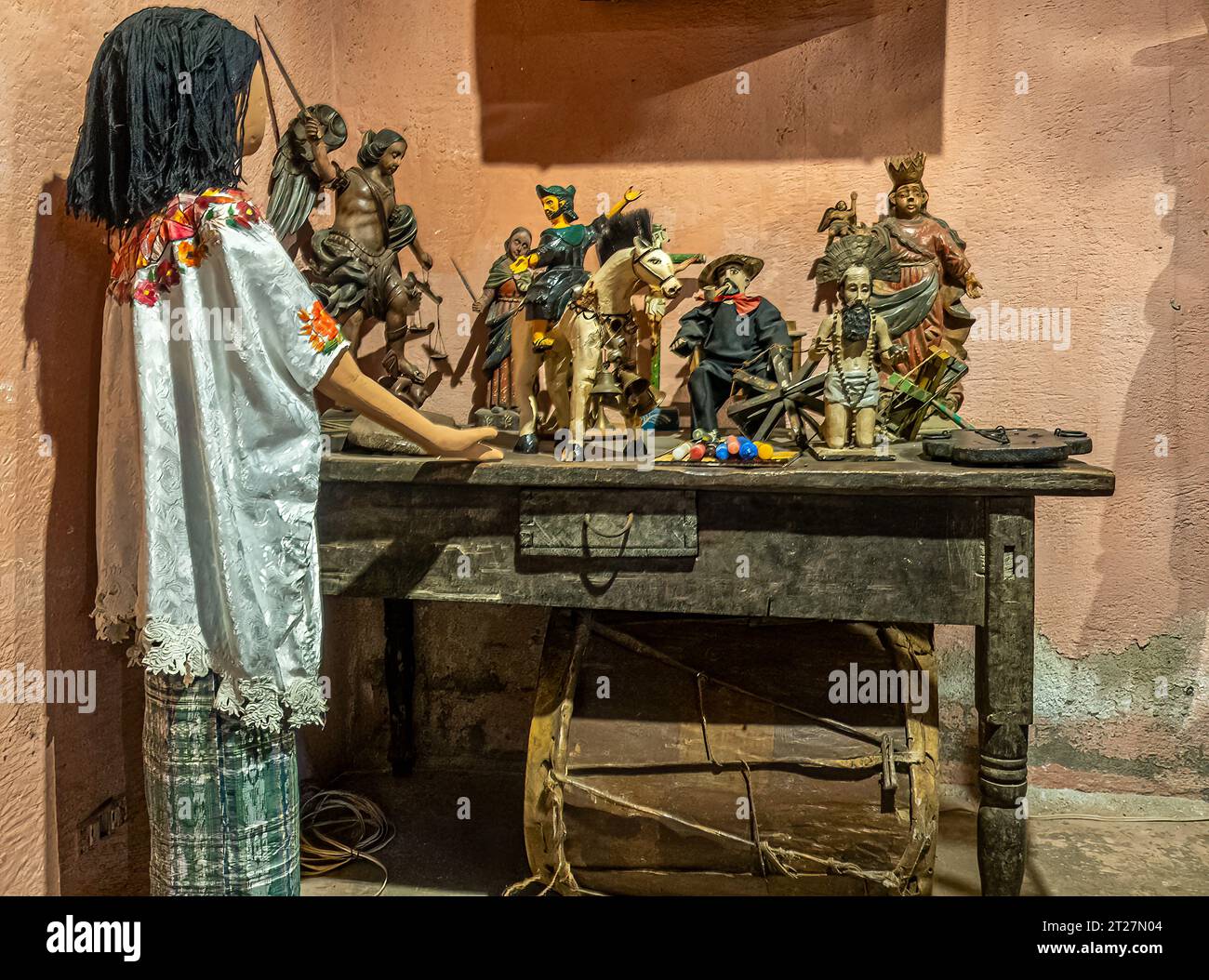 Guatemala, la Antigua - 20 luglio 2023: Musei di Finca la Azotea. Bambola in abito tradizionale che guarda un tavolo pieno di catamarano cattolico Foto Stock