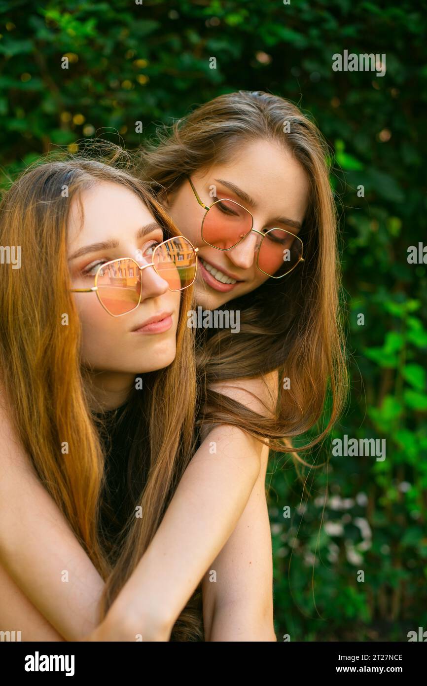 Le giovani sorelle gemelle della generazione Zsnuggono con gli occhiali da sole in un parco, mentre le donne posano fuori. Concetto di amicizia Happy Girls abbracciare Foto Stock