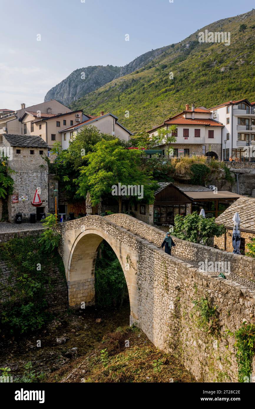 Una donna musulmana sta camminando sul Kriva Cuprija (Ponte Crooked) sul fiume Radobolja, un piccolo e vecchio ponte in pietra a Mostar, Bosnia ed Herzego Foto Stock