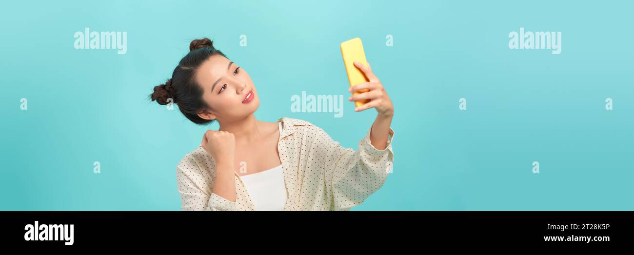 Allegra donna asiatica che tiene lo smartphone con i pugni stringuti per celebrare la vittoria che esprime il successo Foto Stock
