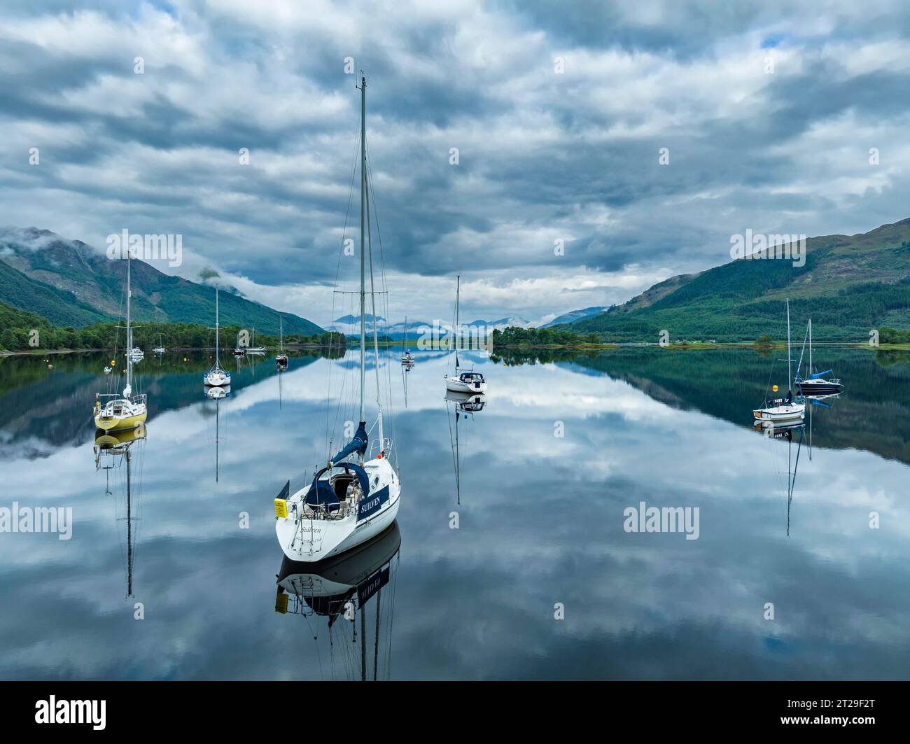 Vista aerea, atmosfera mattutina con riflessi d'acqua sul lago di loch Leven di acqua dolce, con barche a vela parcheggiate sulla riva del villaggio di Glen Coe Foto Stock