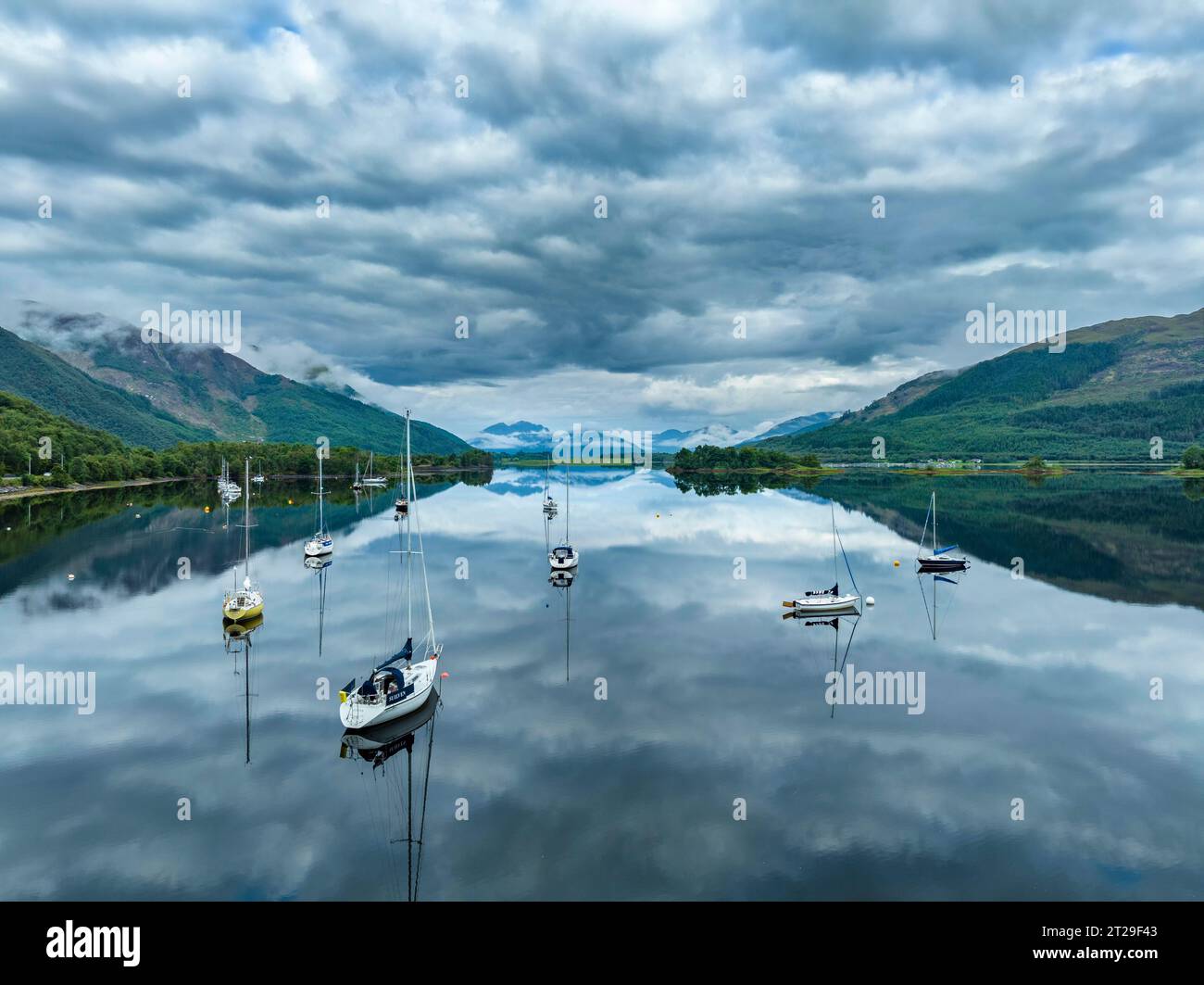 Vista aerea, atmosfera mattutina con riflessi d'acqua sul lago di loch Leven di acqua dolce, con barche a vela parcheggiate sulla riva del villaggio di Glen Coe Foto Stock