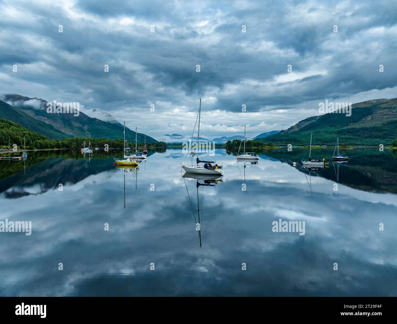 Vista aerea, atmosfera mattutina con riflessi d'acqua sul lago di loch Leven di acqua dolce, con barche a vela parcheggiate sulla riva del villaggio di Glen Coe Foto Stock