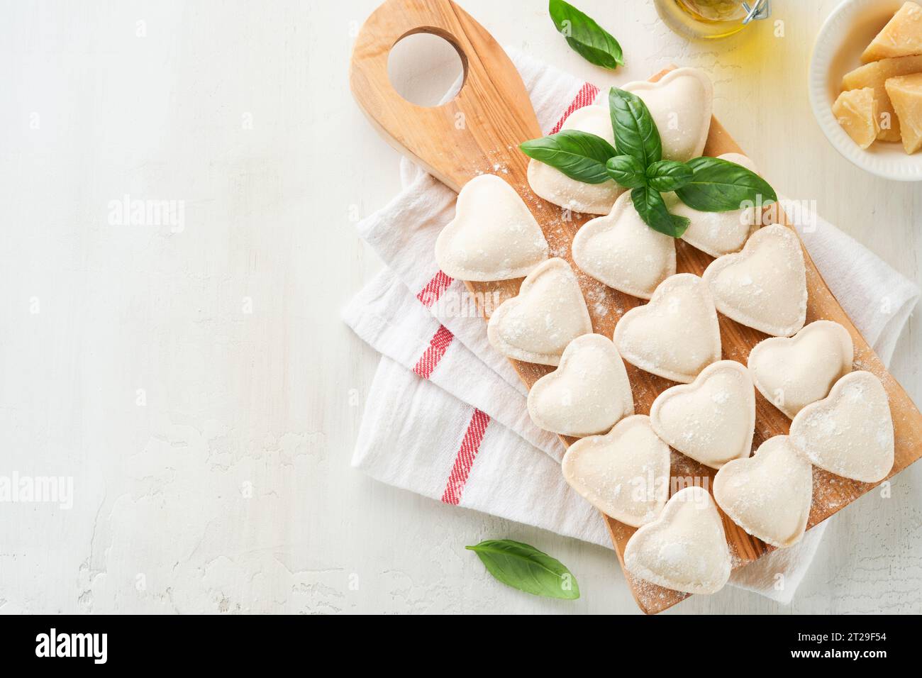 Ravioli italiani a forma di cuore. Gustosi ravioli crudi con farina e basilico su sfondo bianco. Ingredienti per la cottura degli alimenti sfondo. Valentines o M. Foto Stock