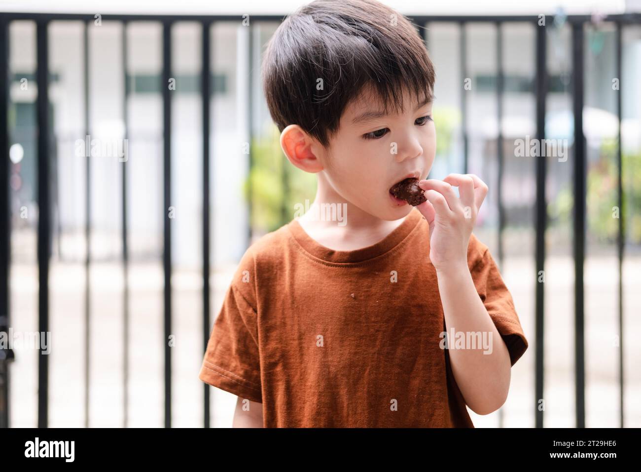Faccia felice del ragazzo asiatico che mangia caramelle al cioccolato Foto Stock