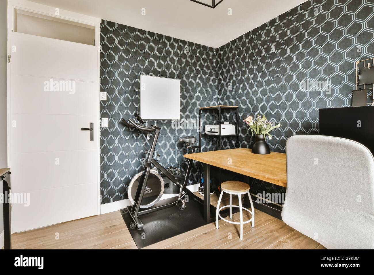 Camera spaziosa con scrivania in legno e cyclette in una casa contemporanea con carta da parati nera e porta chiusa bianca Foto Stock
