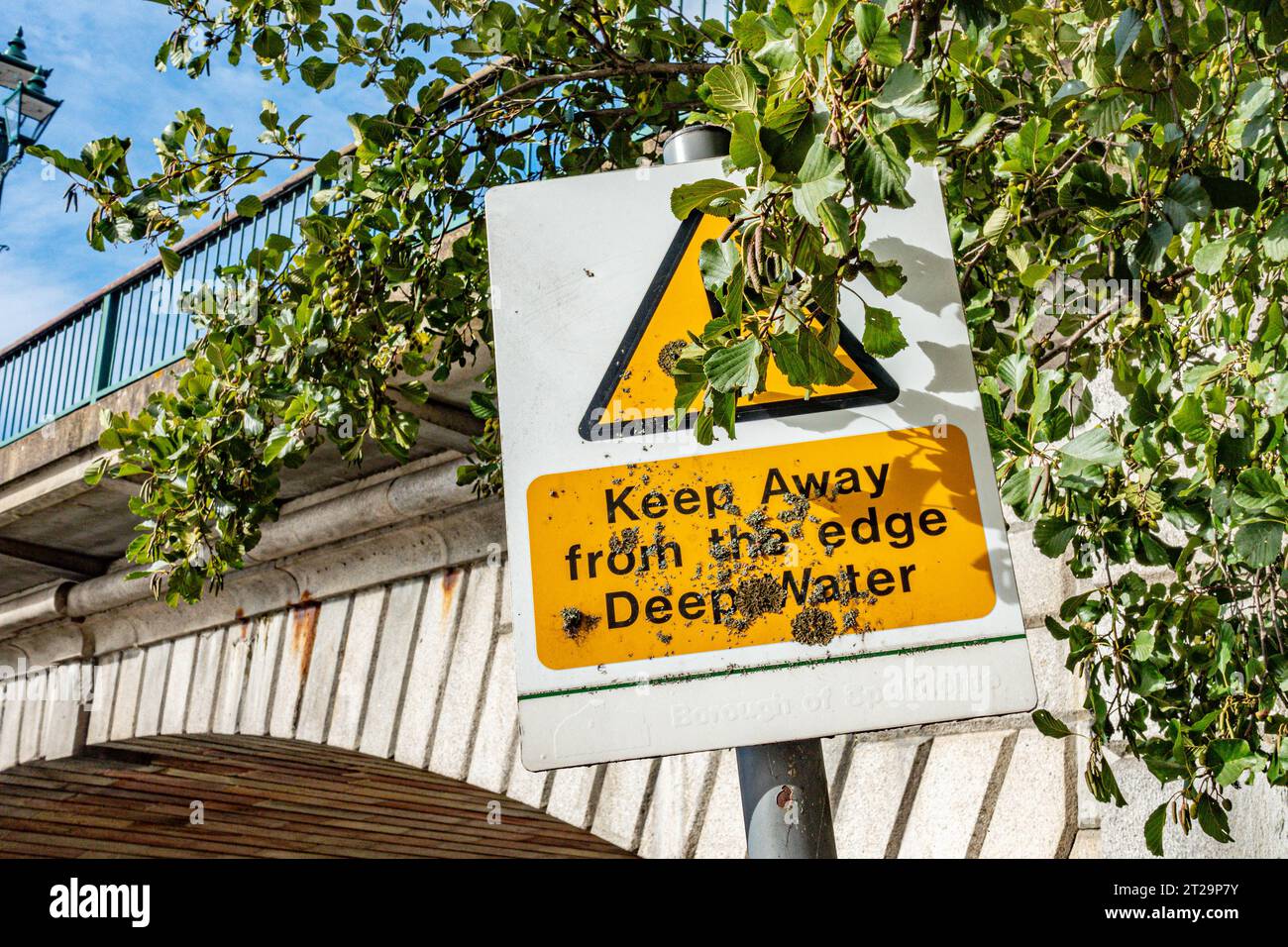 Un cartello del Staines Bridge che avverte del pericolo di acque profonde è parzialmente oscurato da un ramo di un albero Foto Stock