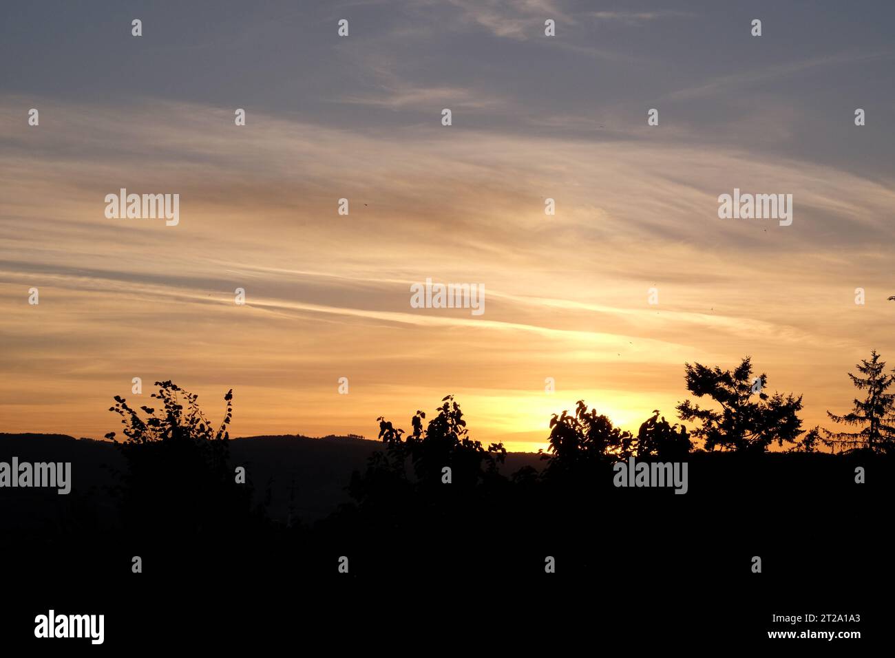 Soffici nubi arancioni in un cielo azzurro con alberi e colline della campagna francese in silhouette; le Bois-d'Oingt e Bagnols, Francia Foto Stock