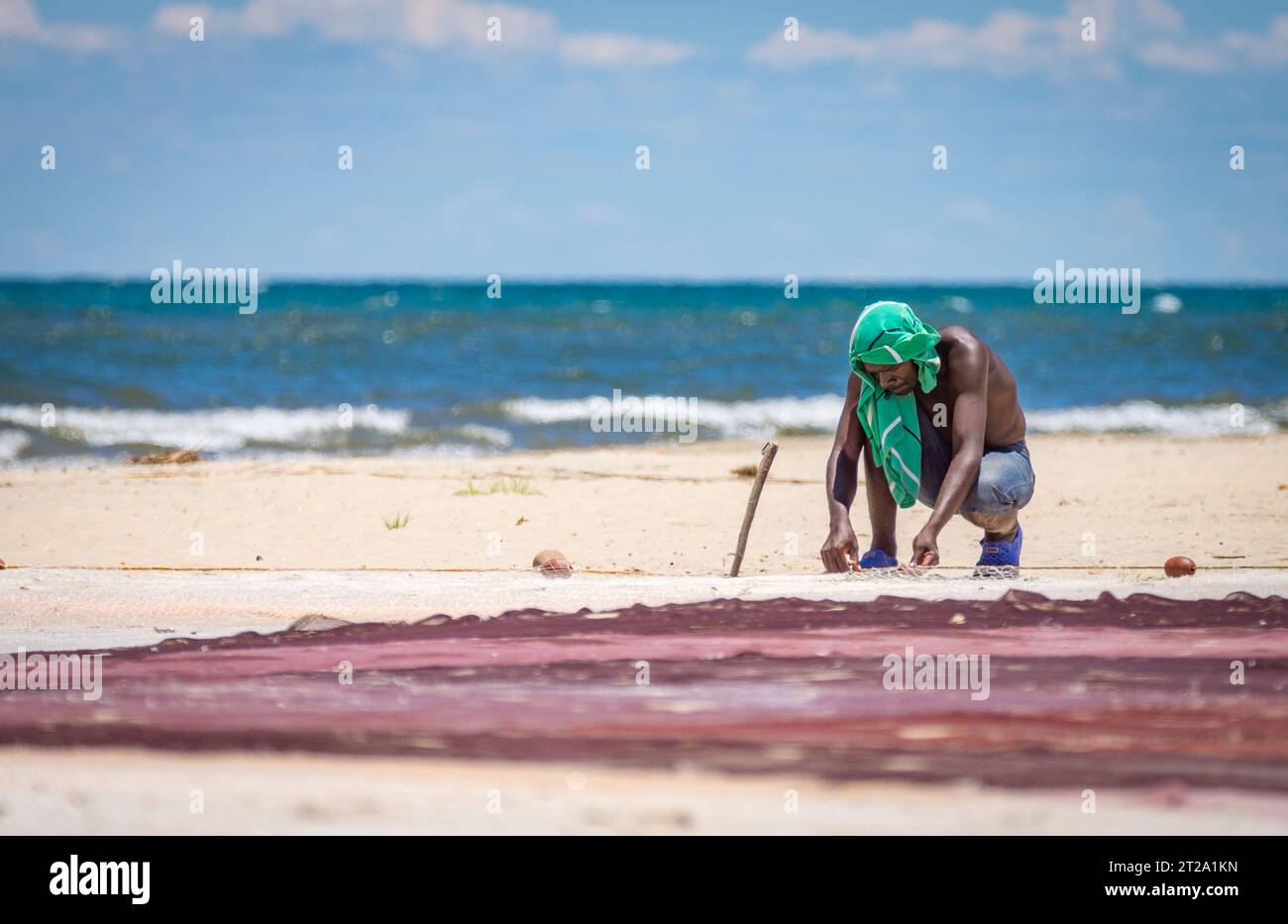 Un uomo sulla riva del lago Malawi mende la sua rete da pesca nel caldo di mezzogiorno. Foto Stock