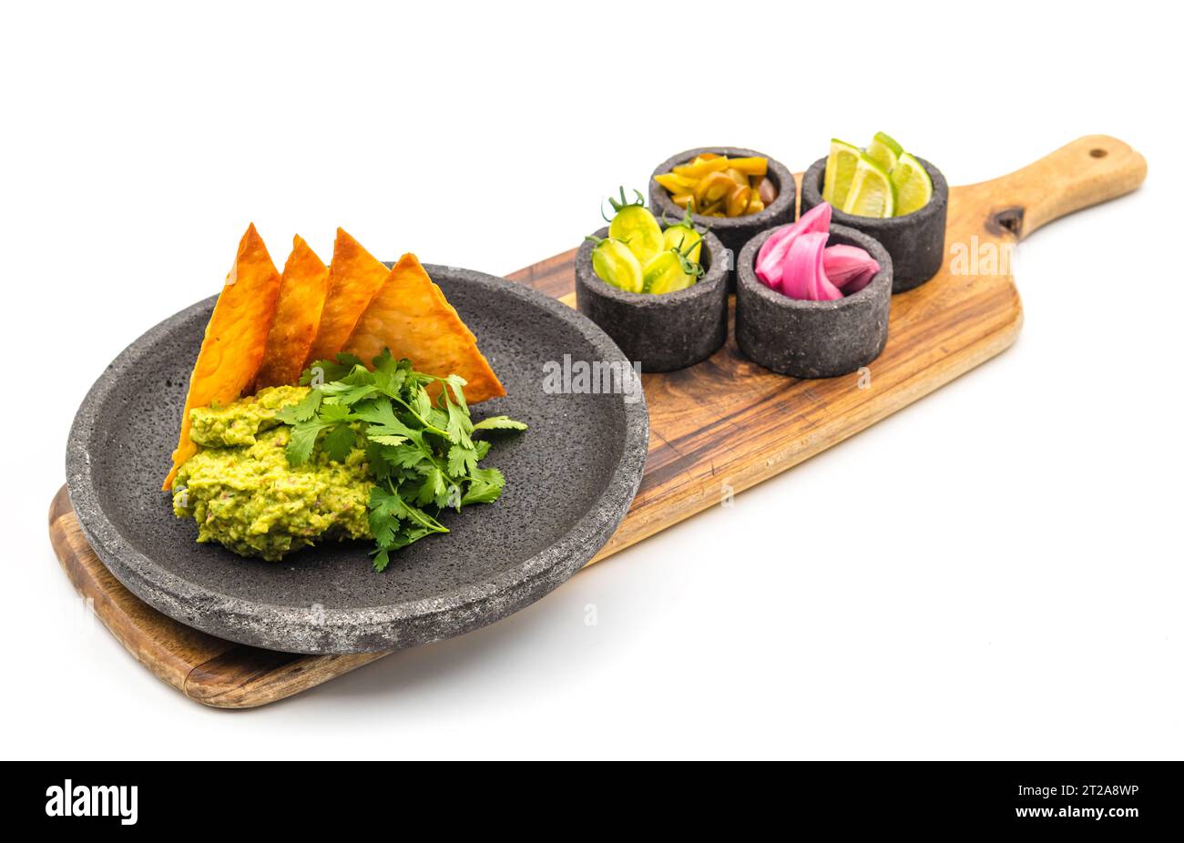 Guacamole all'avocado con tortillas croccanti su un piatto di pietra nera su sfondo bianco Foto Stock