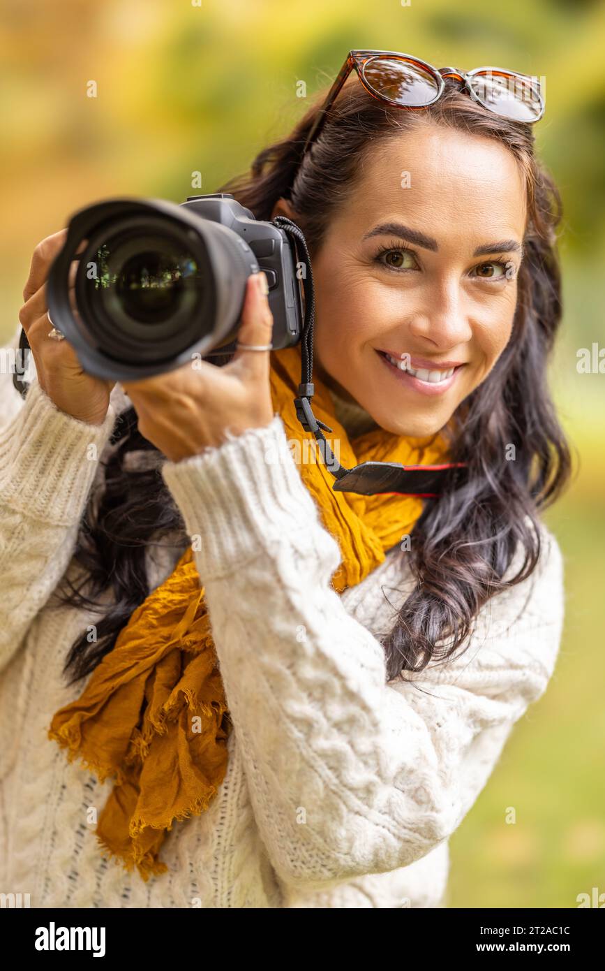 Bella donna con una macchina fotografica professionale e alla ricerca di composizione nella natura autunnale, sorride. Foto Stock