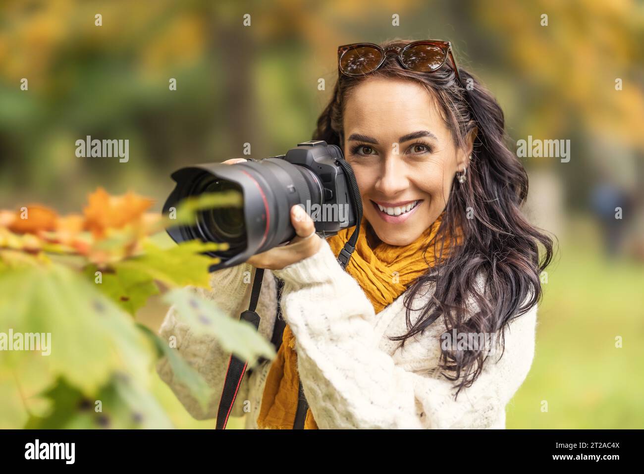 Bella donna con una macchina fotografica professionale e alla ricerca di composizione nella natura autunnale, sorride. Foto Stock