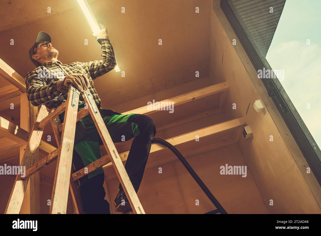 Lavoratore elettricista appaltatore che installa una barra LED all'interno di un piccolo capannone in legno moderno Foto Stock