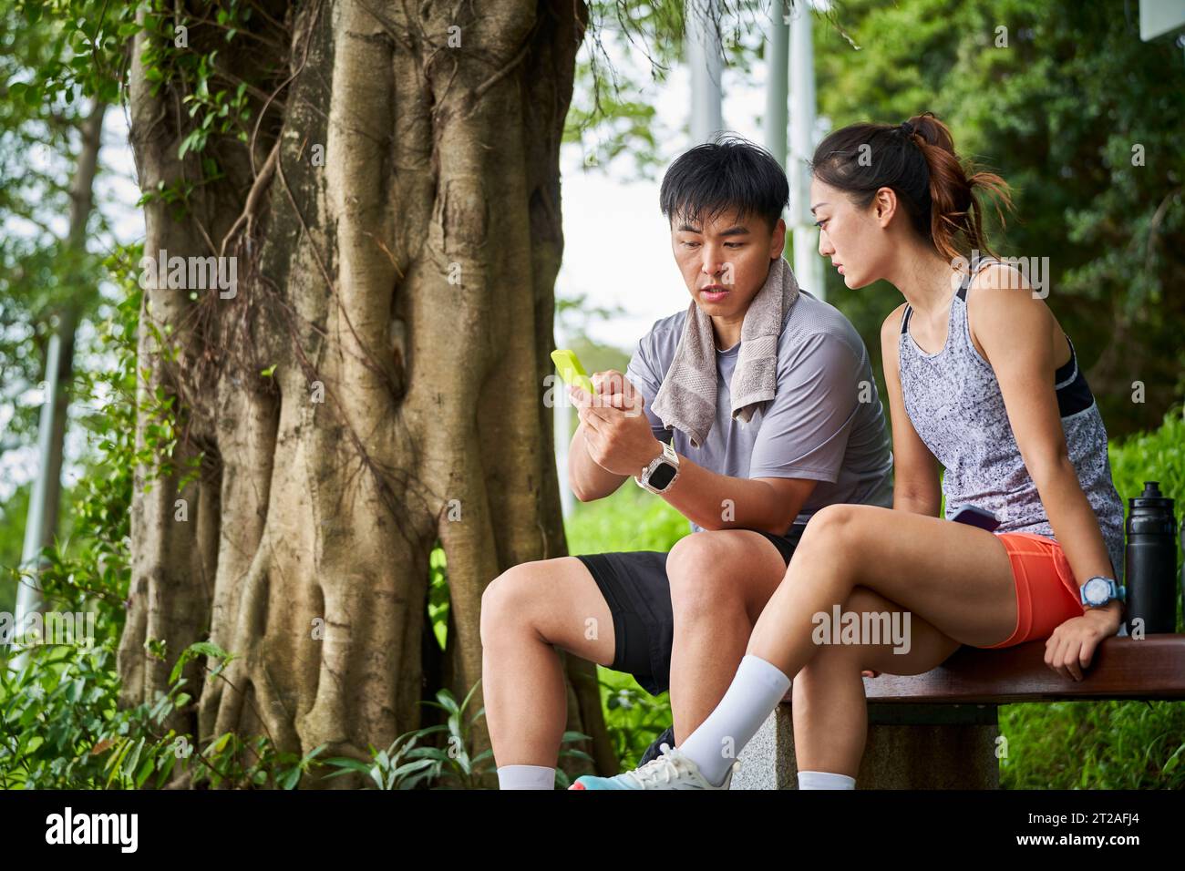 giovane coppia asiatica che guarda il cellulare mentre fa una pausa durante l'esercizio all'aperto Foto Stock