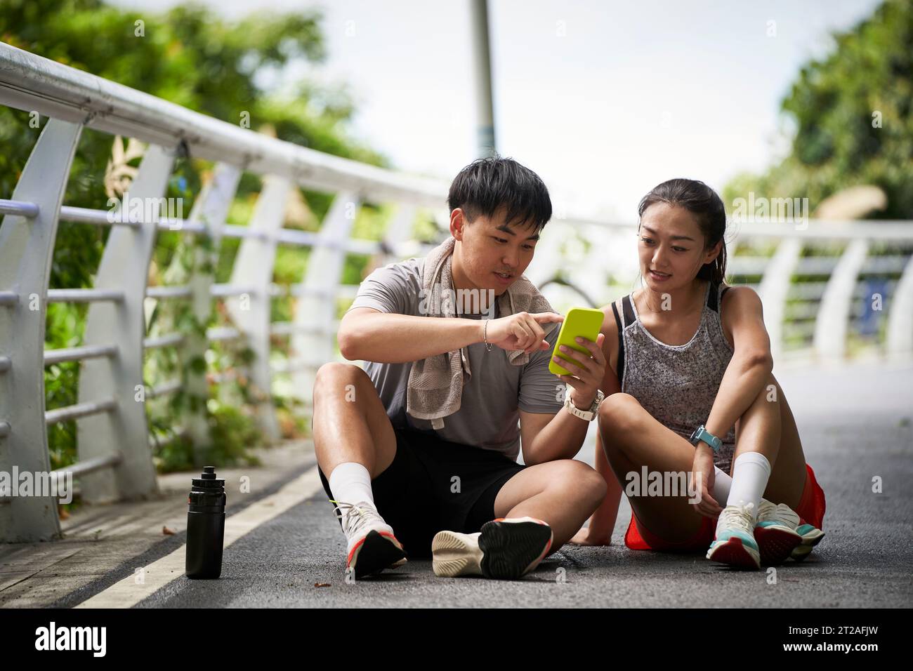 giovane coppia asiatica che guarda le foto del cellulare mentre fa una pausa durante gli esercizi all'aperto Foto Stock