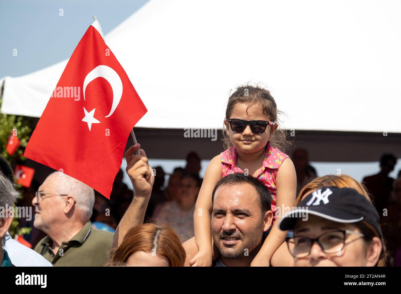 Izmir, Turchia, 9 settembre 2023: Un momento commovente che cattura una ragazza di 8-9-year-Old con gli occhiali da sole, appollaiata sulle spalle di suo padre, salutando Foto Stock